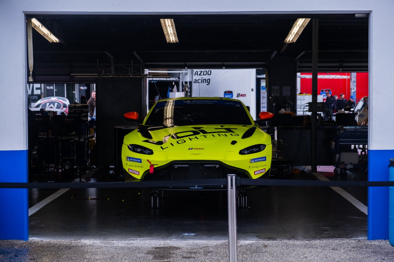 A vibrant yellow race car in a garage workshop with mechanics in the background.